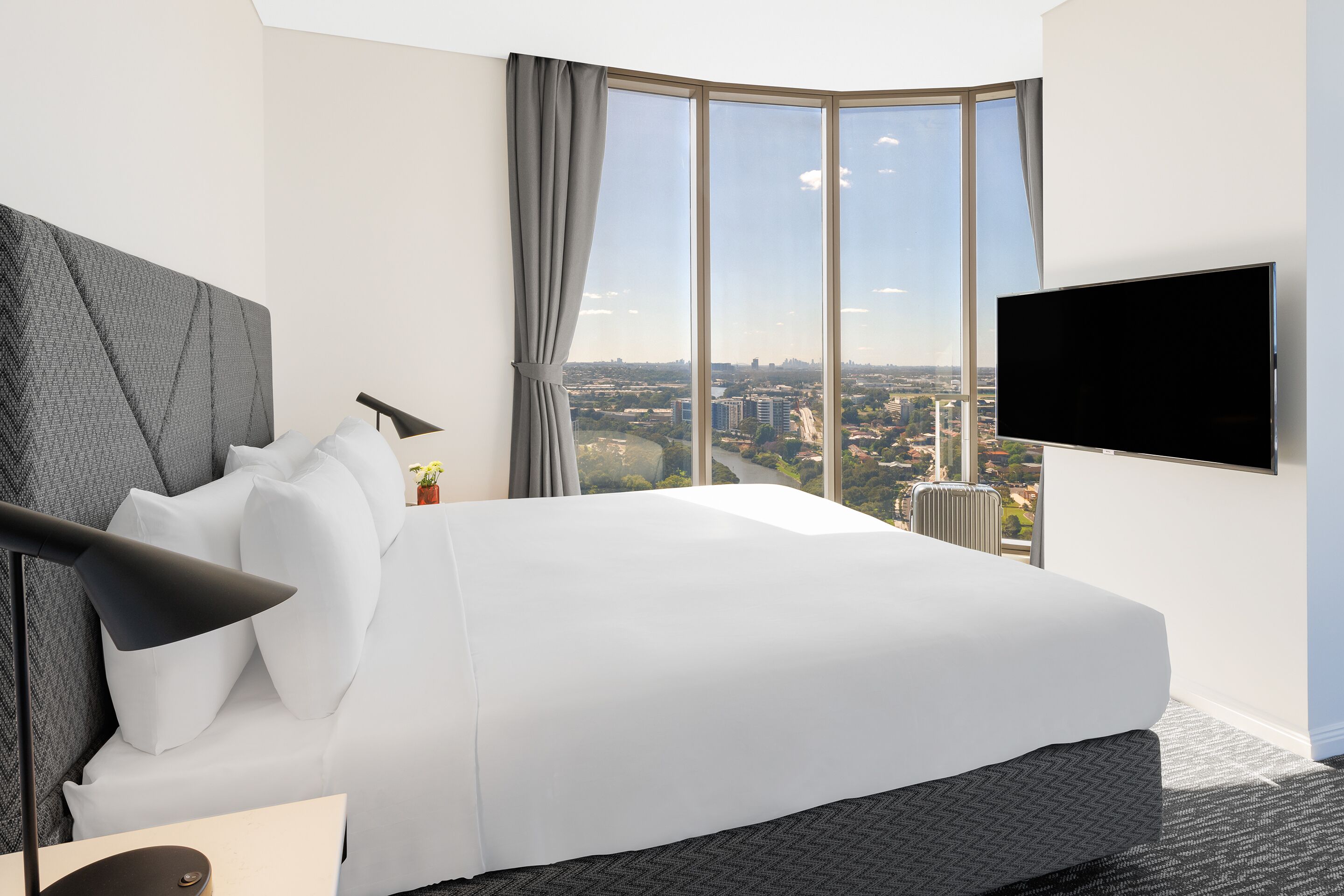 A hotel room with a large bed, a flat-screen TV, a view of the city, and a modern design.