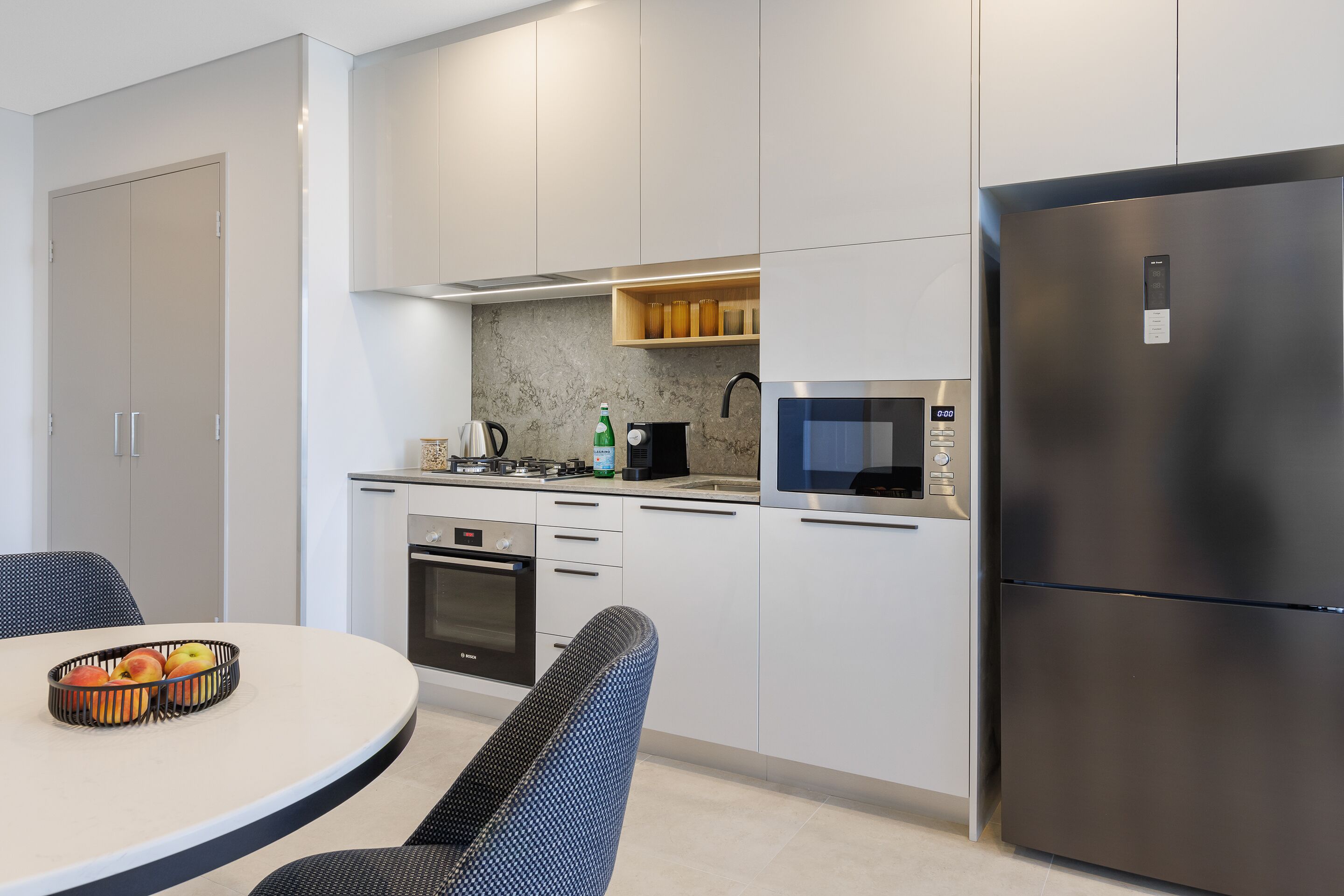 A modern kitchen with white cabinets, a stainless steel refrigerator, a microwave, and a built-in oven.