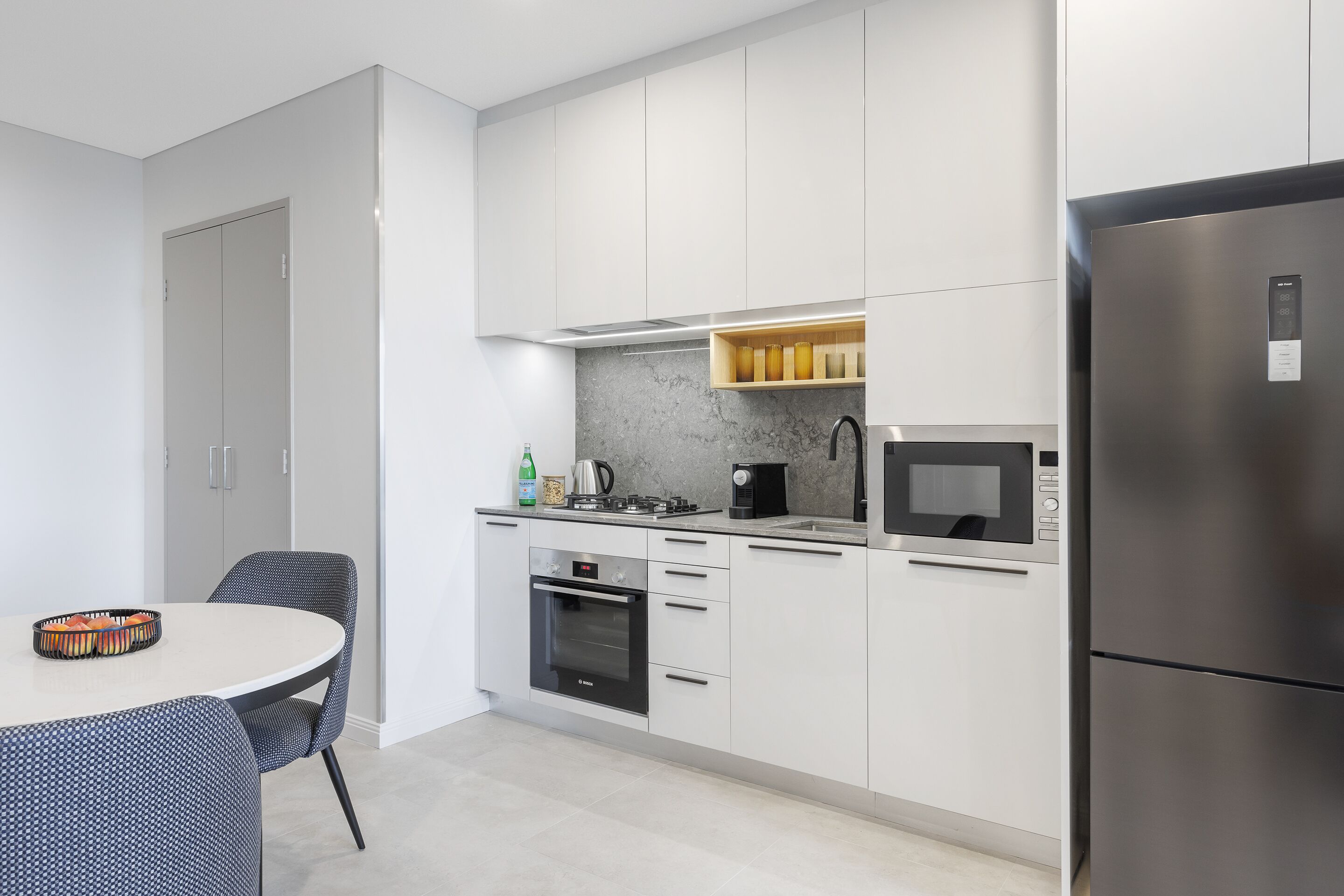 A modern kitchen with white cabinets, a stainless steel refrigerator, a built-in oven, and a microwave.