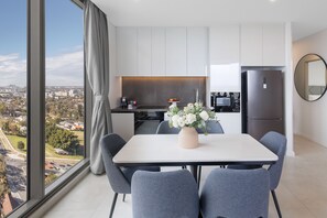 A modern kitchen with white cabinets, a stainless steel refrigerator, and a dining area with a table and chairs. - Meriton Suites George Street, Parramatta (Parramatta)