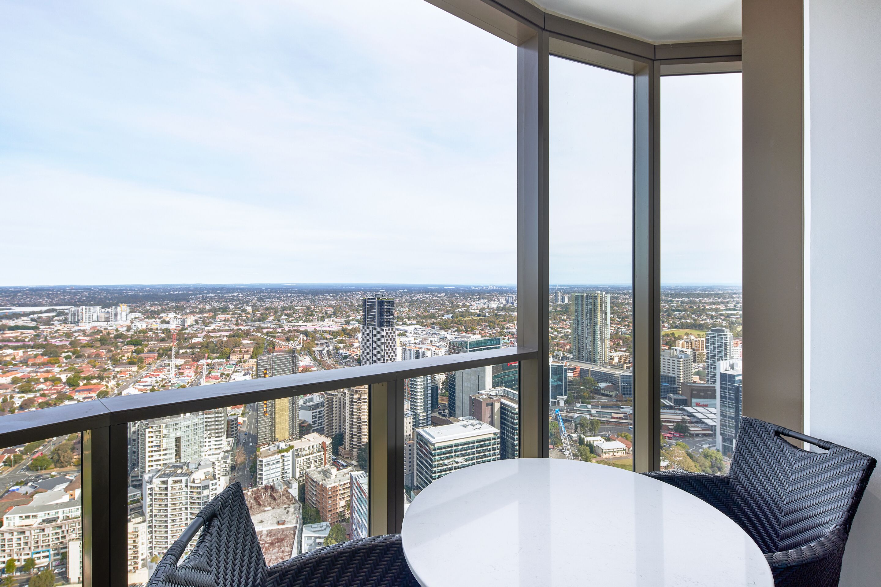 A high-rise room with a panoramic city view, a round table, and wicker chairs.