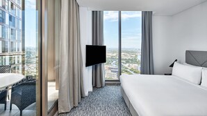 Ein Hotelzimmer mit einem großen Bett, einem an der Wand befestigten Fernseher, einem Balkon mit Blick auf die Stadt und einem Essbereich mit Tisch und Stühlen.