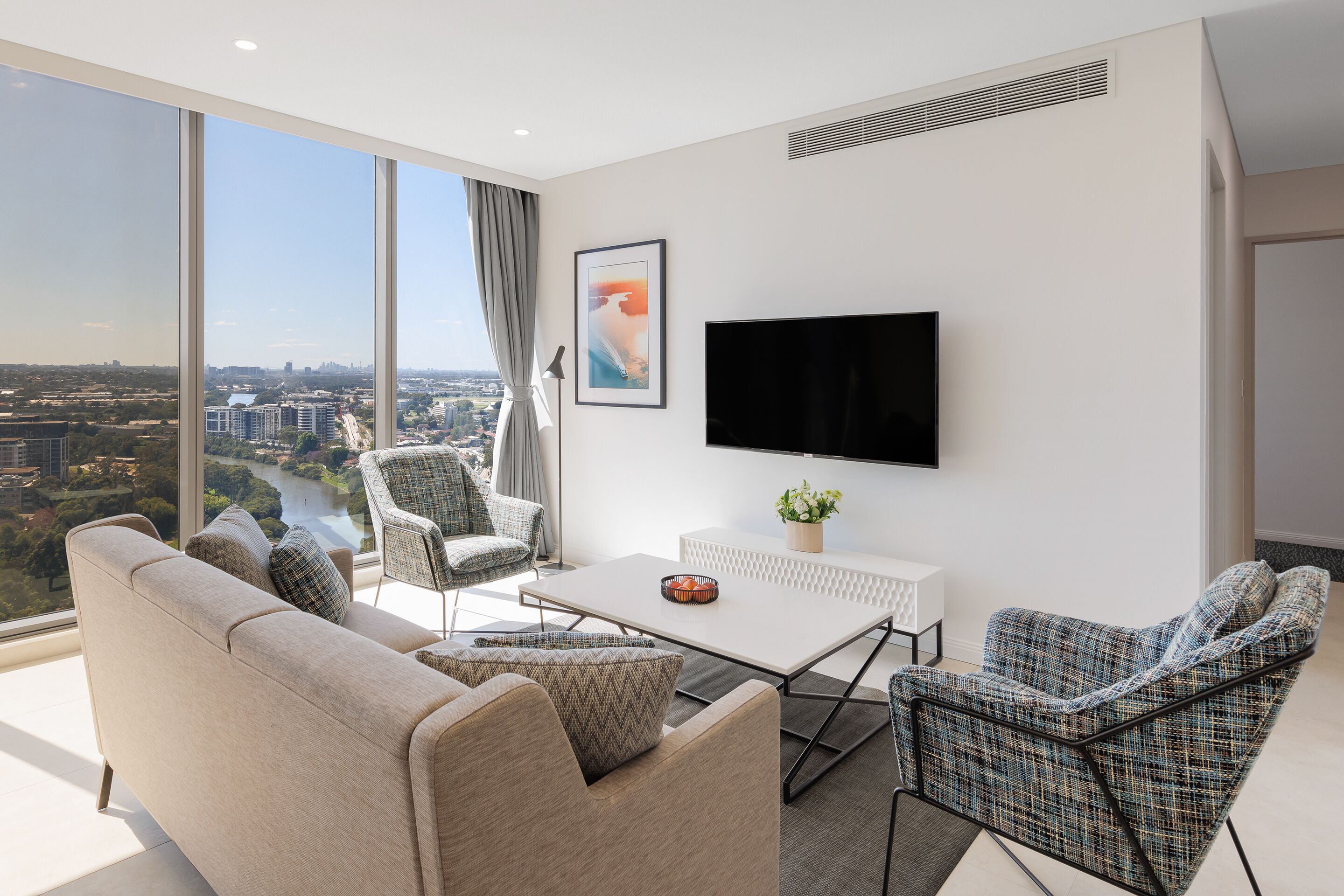 A modern living room with a large window, a flat-screen TV, and a sofa.