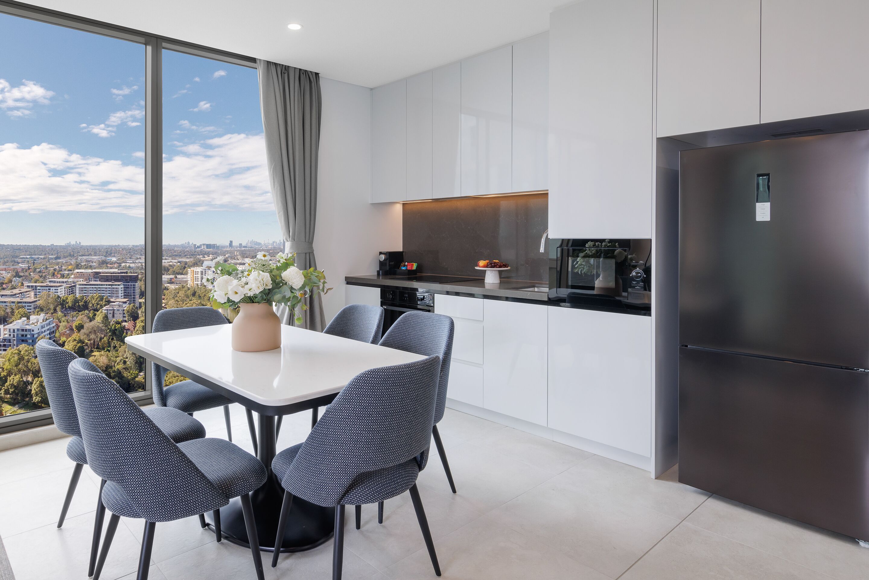 Een moderne keuken met een grote koelkast, witte kasten en een eethoek met een tafel en stoelen.