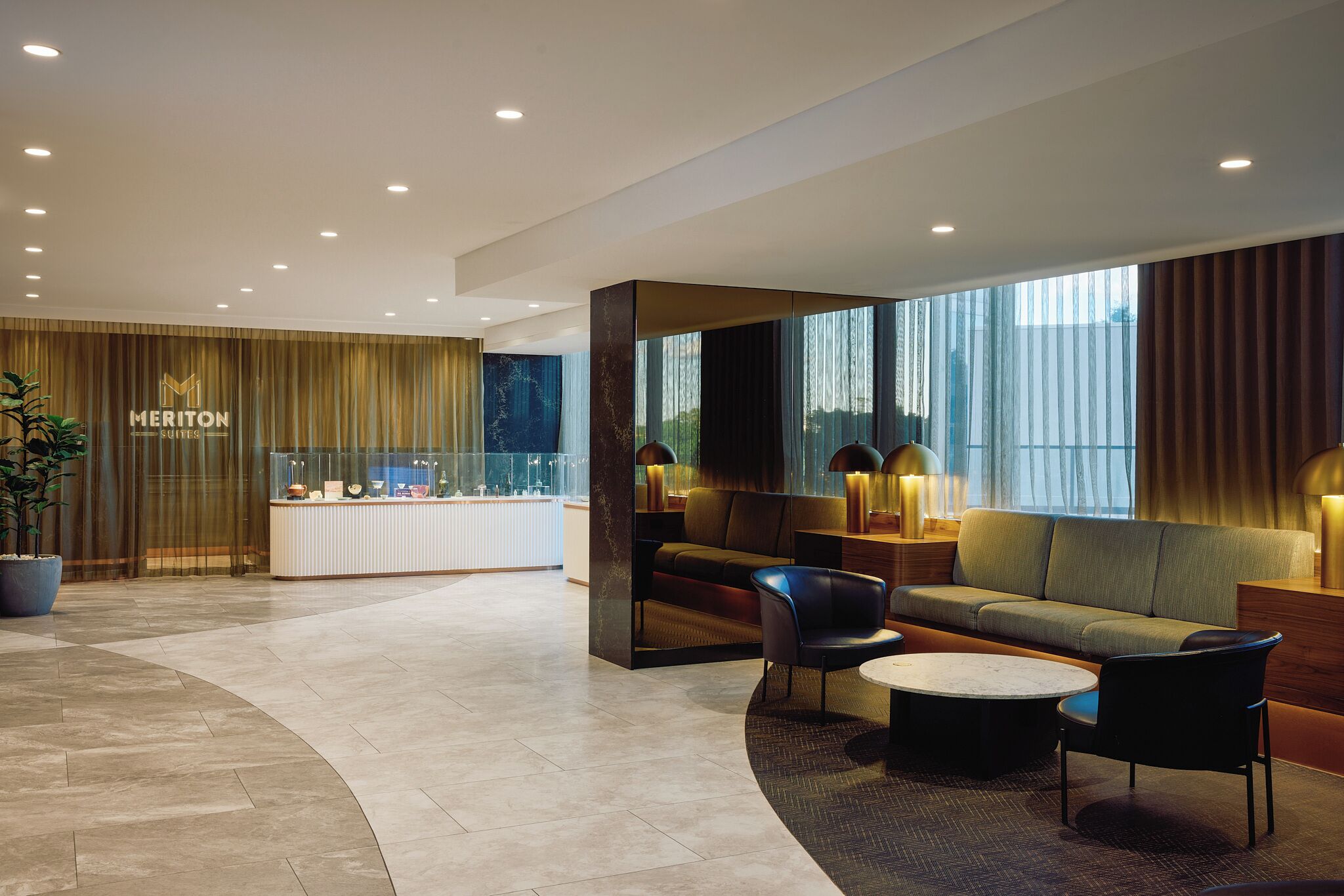 A modern hotel lobby with a reception desk, seating area, and large windows.