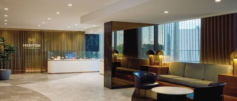 A modern hotel lobby with a reception desk, seating area, and large windows.