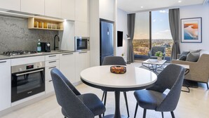 Eine moderne Küche mit einem Bosch-Backofen, ein Essbereich mit einem runden Tisch und Stühlen sowie ein Wohnbereich mit einer Couch und Blick auf die Stadt.
