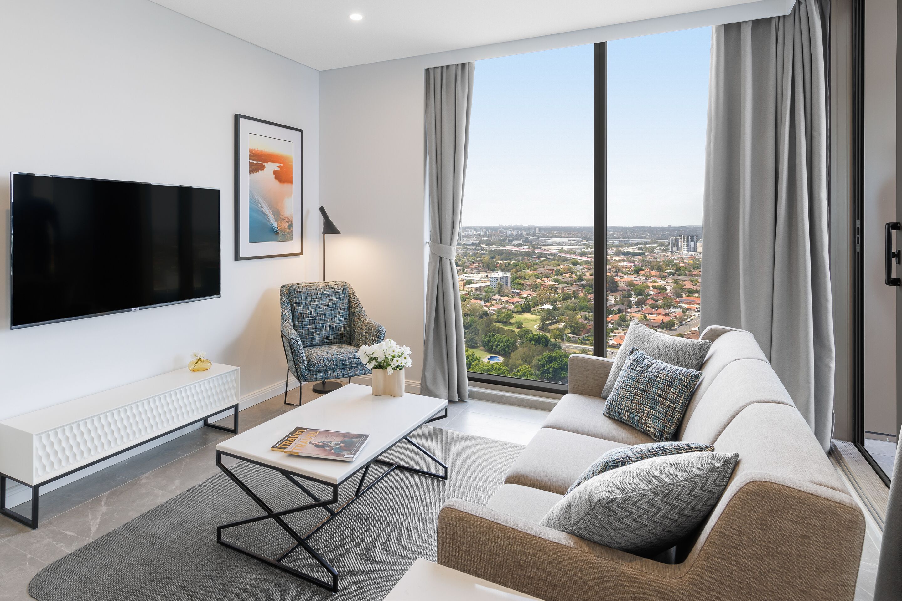 A modern living room with a large TV, a sofa, a coffee table, and a view of a cityscape.