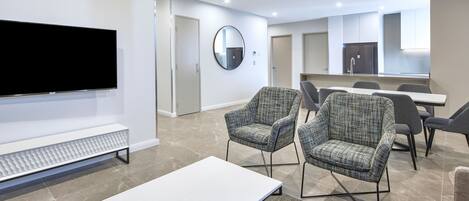 Una habitación de hotel moderna con una televisión de pantalla plana, un espejo redondo y una zona de comedor con sillas y una mesa.