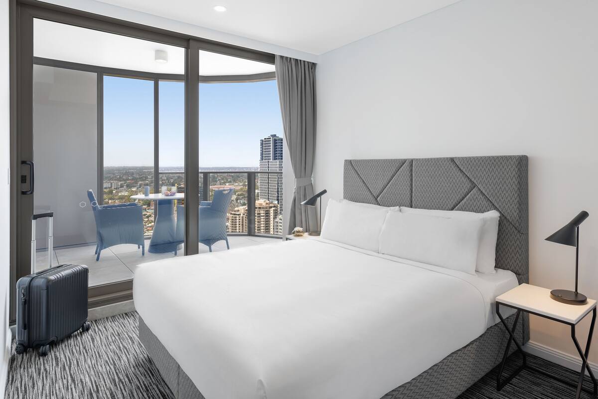 A hotel room with a large bed, a desk, a chair, and a view of the city.