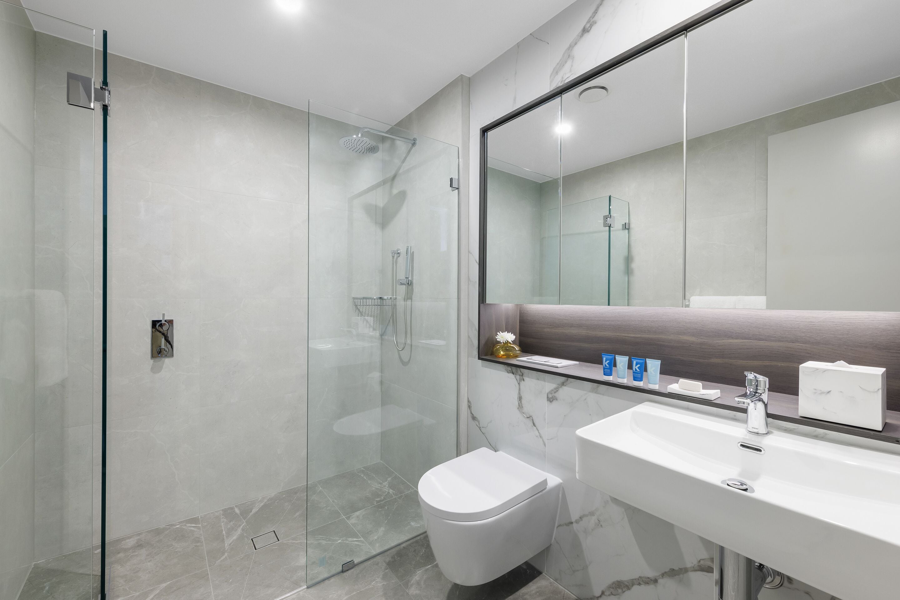 A modern bathroom with a glass-enclosed shower, a white toilet, and a marble-tiled sink area.