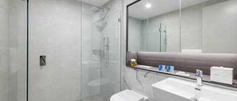A modern bathroom with a glass-enclosed shower, a white toilet, and a marble-tiled sink area.