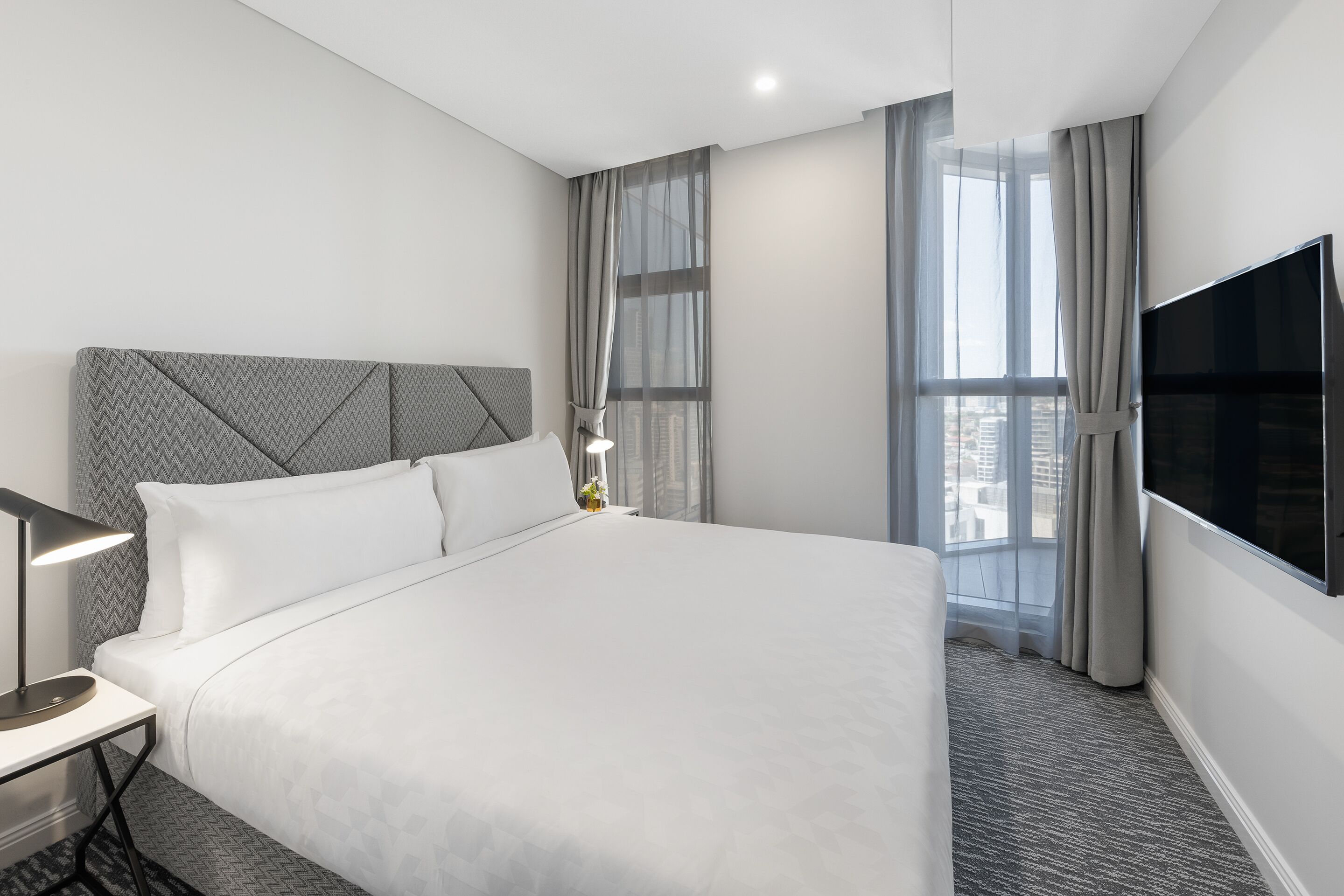 Ein modernes Hotelzimmer mit einem großen Bett, einem Flachbildfernseher und Blick auf die Stadt.