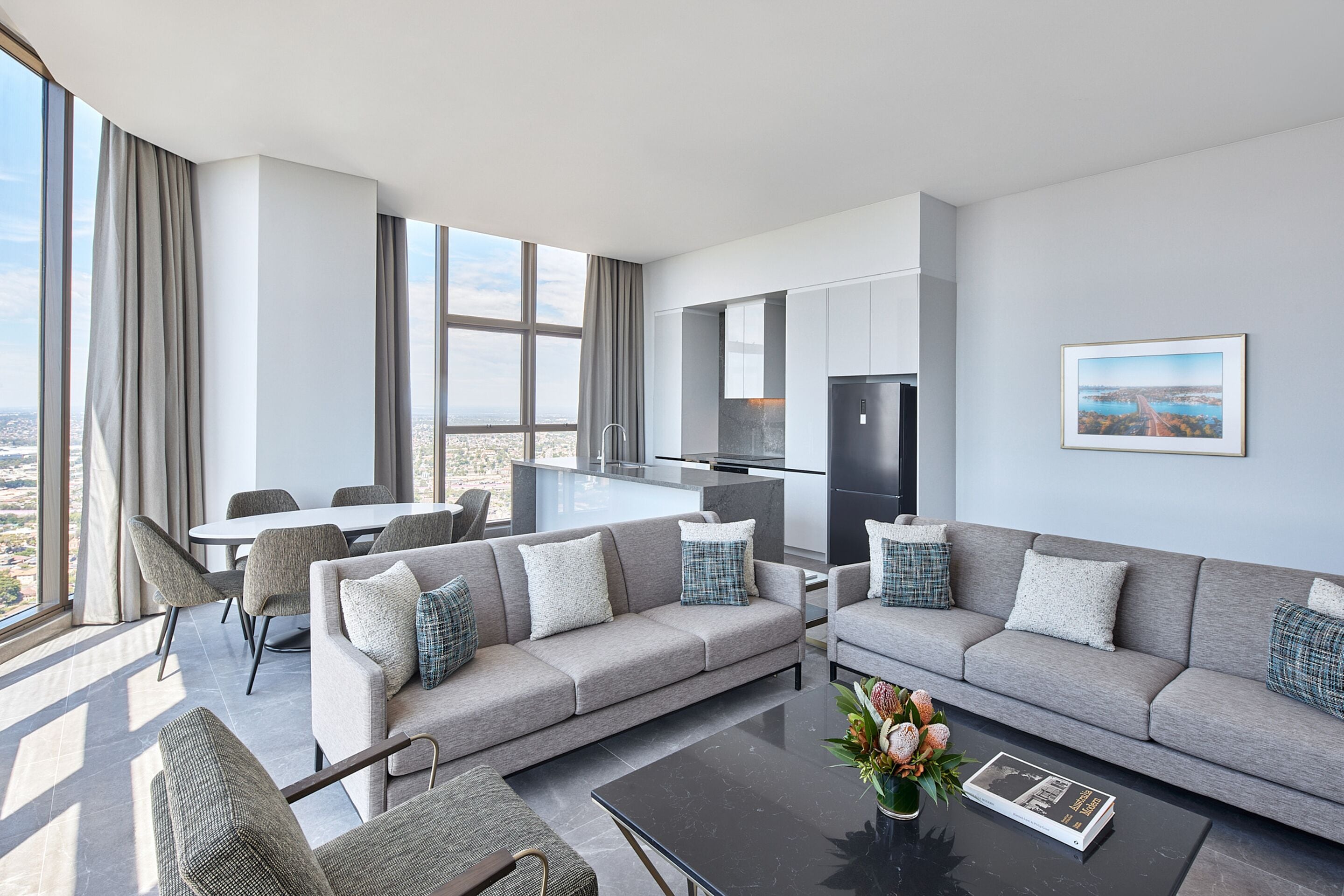 A modern living room with a grey sofa, a coffee table, and a dining area with chairs.