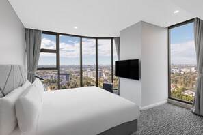 A modern hotel room with a large bed, a flat-screen TV, and a city view through large windows. - Meriton Suites George Street, Parramatta (Parramatta)