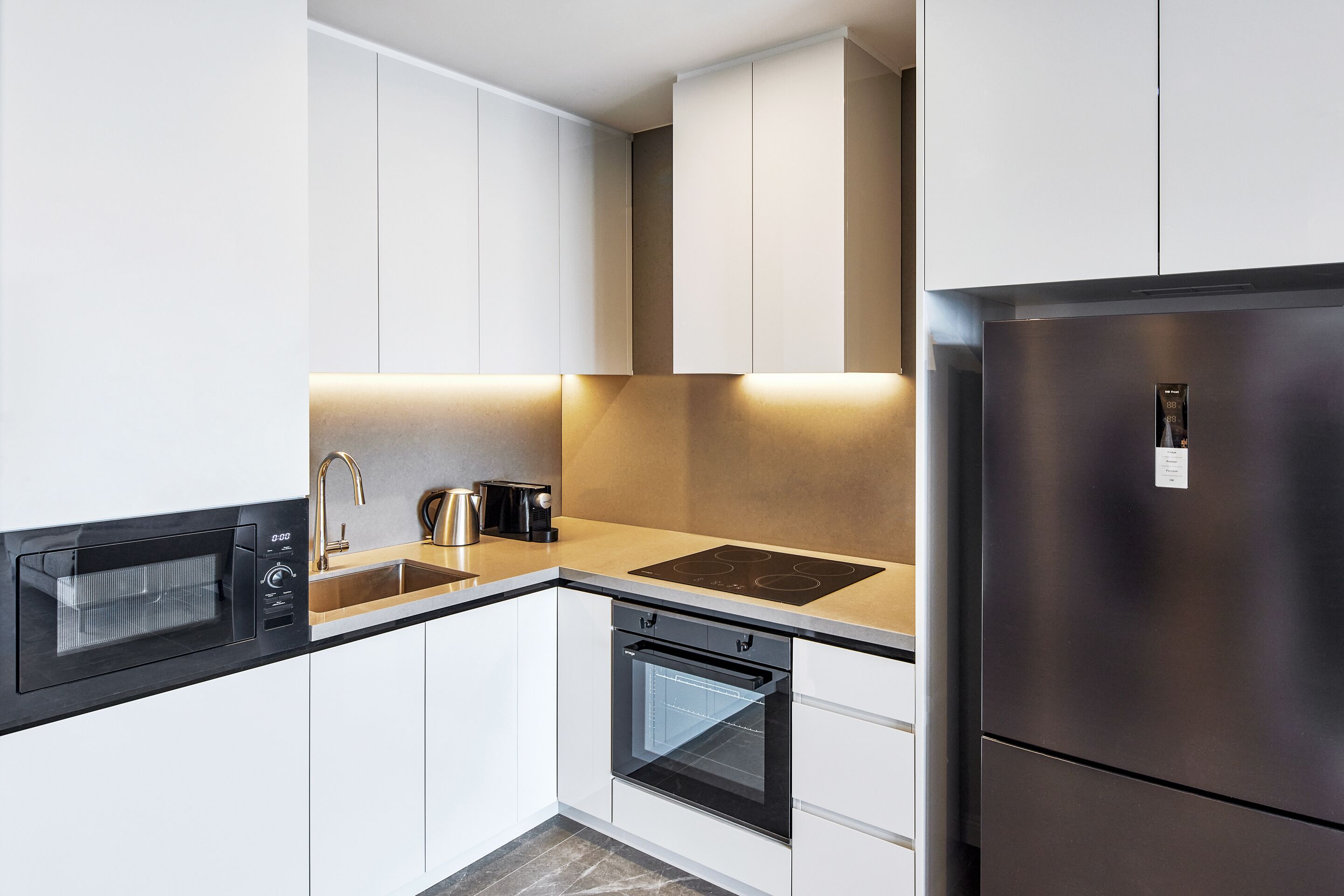 A modern kitchen with white cabinets, a stainless steel refrigerator, a built-in oven, and a microwave.