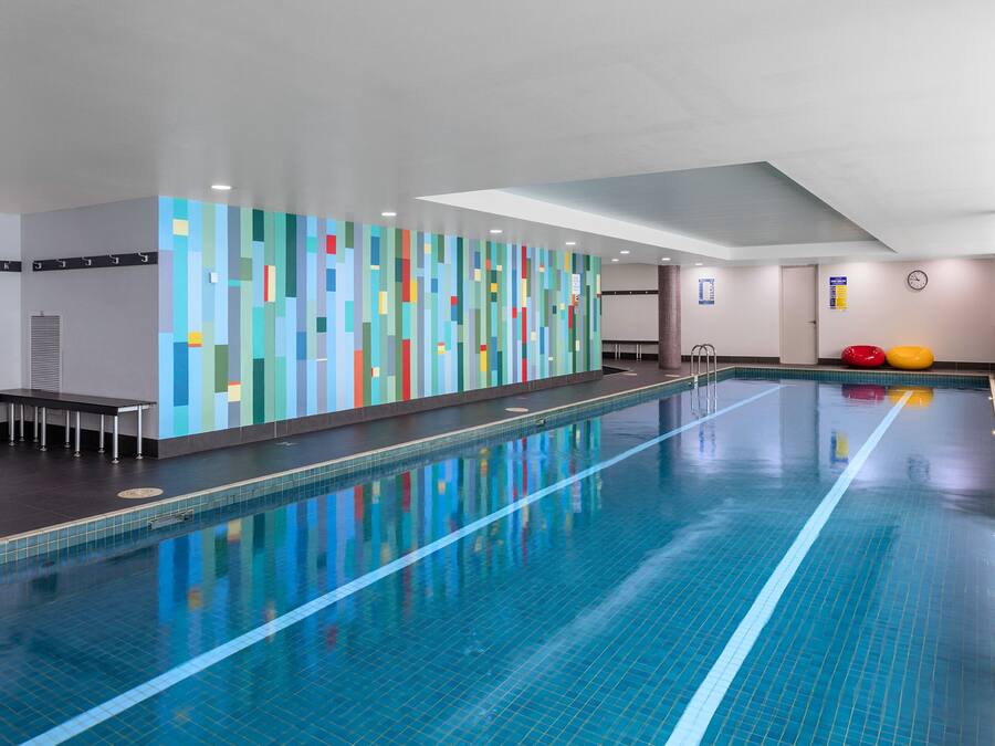 A swimming pool with a tiled floor and walls, a bench along the side, and a colorful wall decoration.