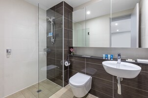 Un baño moderno con ducha de vidrio, inodoro blanco y lavamanos con espejo.