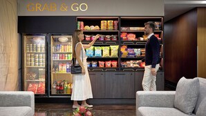 Vestíbulo de hotel con una zona de aperitivos 'GRAB & GO', asientos y suelo de mármol.