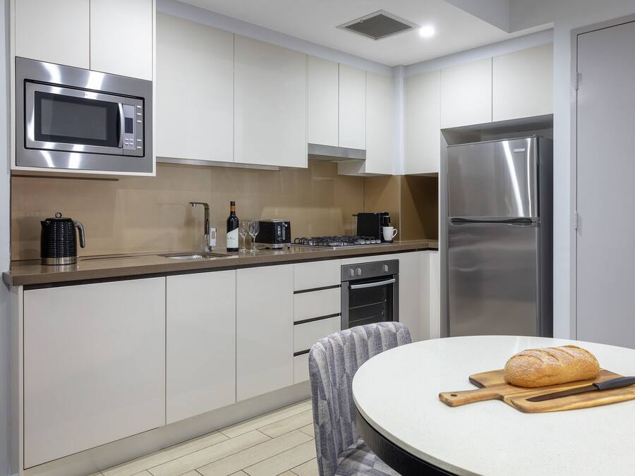 Een moderne keuken met witte kastjes, een roestvrijstalen koelkast, een magnetron en een eethoek met een ronde tafel en een brood.
