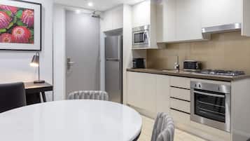 A modern kitchen with stainless steel appliances, a round dining table, and a framed floral artwork on the wall.