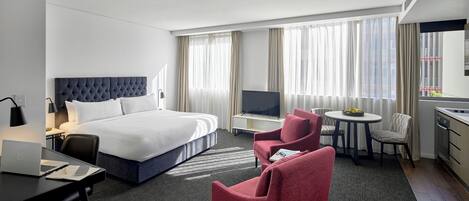 A hotel room with a bed, desk, laptop, TV, two chairs, and a dining table.