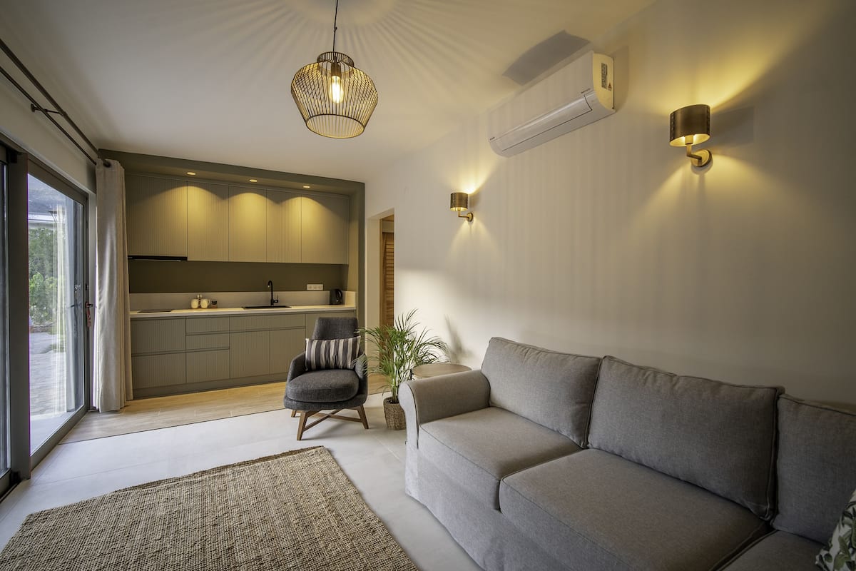 Ein modernes Wohnzimmer mit einem grauen Sofa, einem gemusterten Teppich, einem Holzstuhl und einer Pendelleuchte.