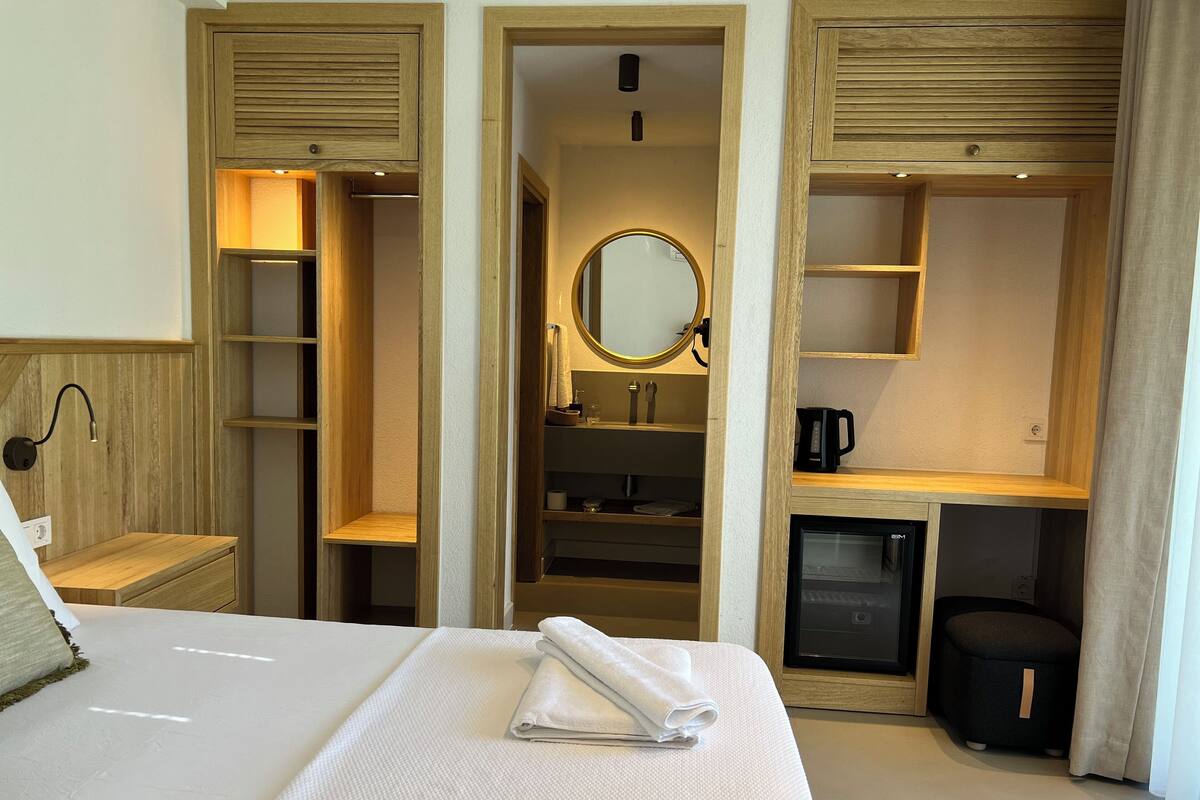 Ein Hotelzimmer mit Bett, Schreibtisch, Spiegel, einer kleinen Küchenzeile und fest eingebauten Regalen.