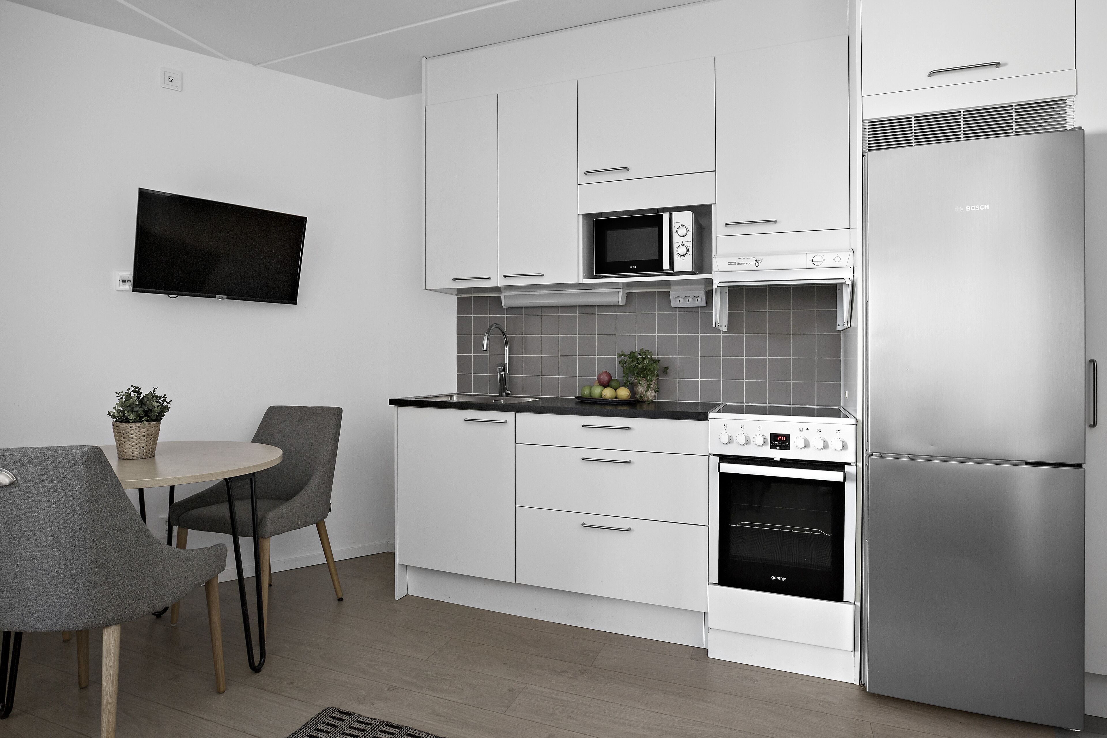 Une cuisine moderne avec des meubles blancs, un réfrigérateur Bosch, un four à micro-ondes et une cuisinière. On y trouve également un coin repas avec une table et des chaises.