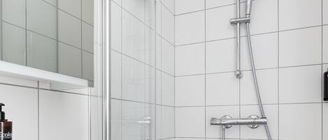 Un baño moderno con cabina de ducha de vidrio, un lavabo blanco y una pequeña planta en maceta.