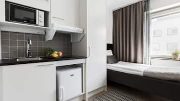 A compact kitchen with a microwave, refrigerator, and sink. A small dining area with a bench and a window with curtains.
