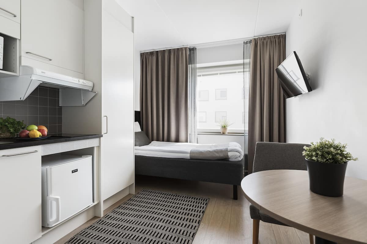 Une chambre d’hôtel compacte comprenant un coin cuisine, un lit, une table à manger et une plante en pot.