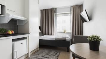 Una habitación de hotel compacta con kitchenette, una cama, una mesa de comedor y una planta en maceta.