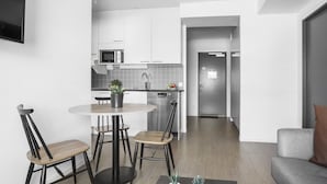 Eine moderne Küche mit weißen Schränken, einer Mikrowelle und einem Spülbecken. Es gibt einen Essbereich mit einem runden Tisch und Stühlen sowie ein Wohnzimmer mit einer Couch und einem Couchtisch.