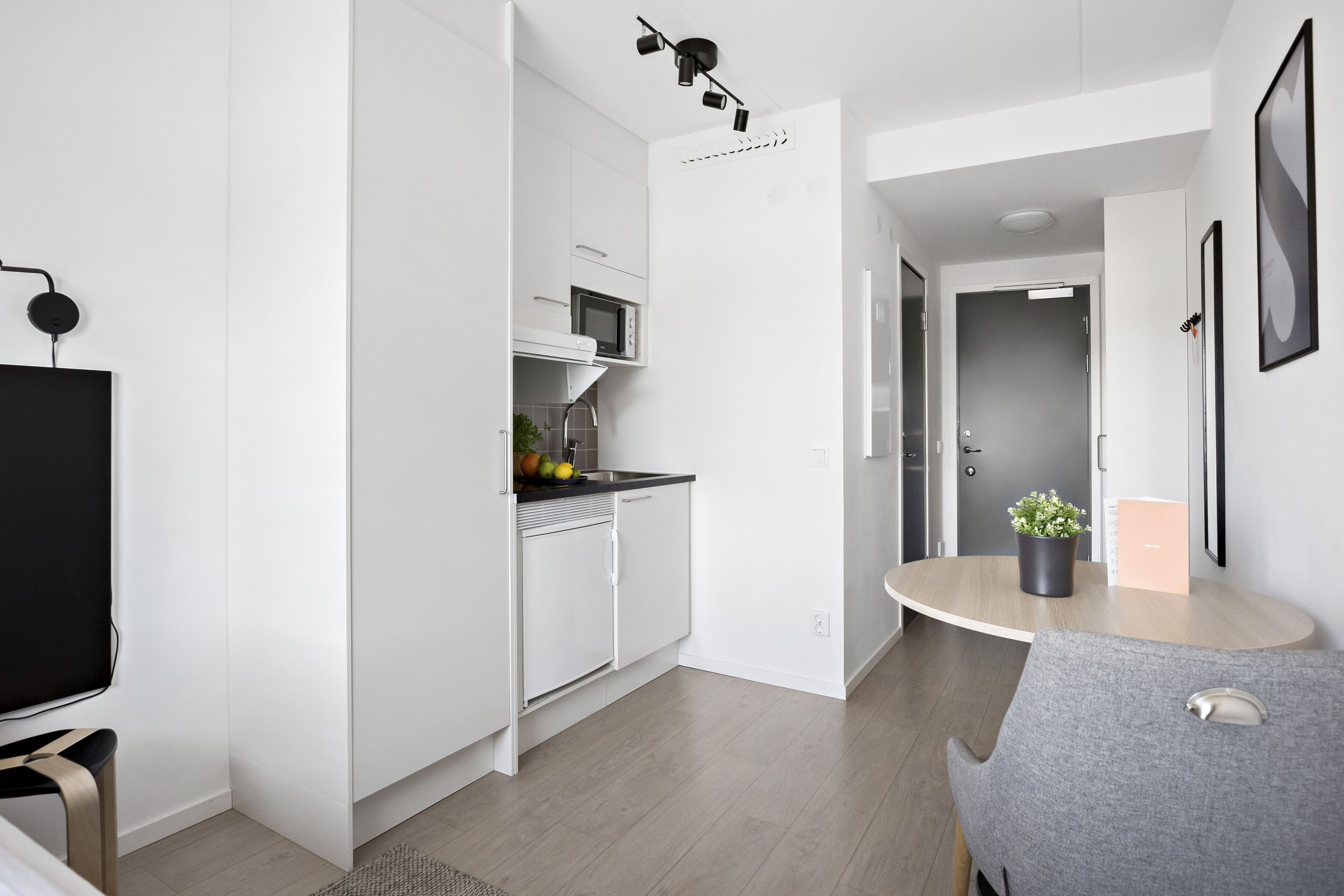 A modern kitchen with white cabinets, a microwave, and a sink. There is a dining area with a round table and a chair.
