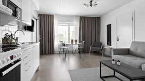 Eine moderne Küche mit weißen Geräten, ein Essbereich mit Tisch und Stühlen und ein graues Sofa im Wohnbereich.