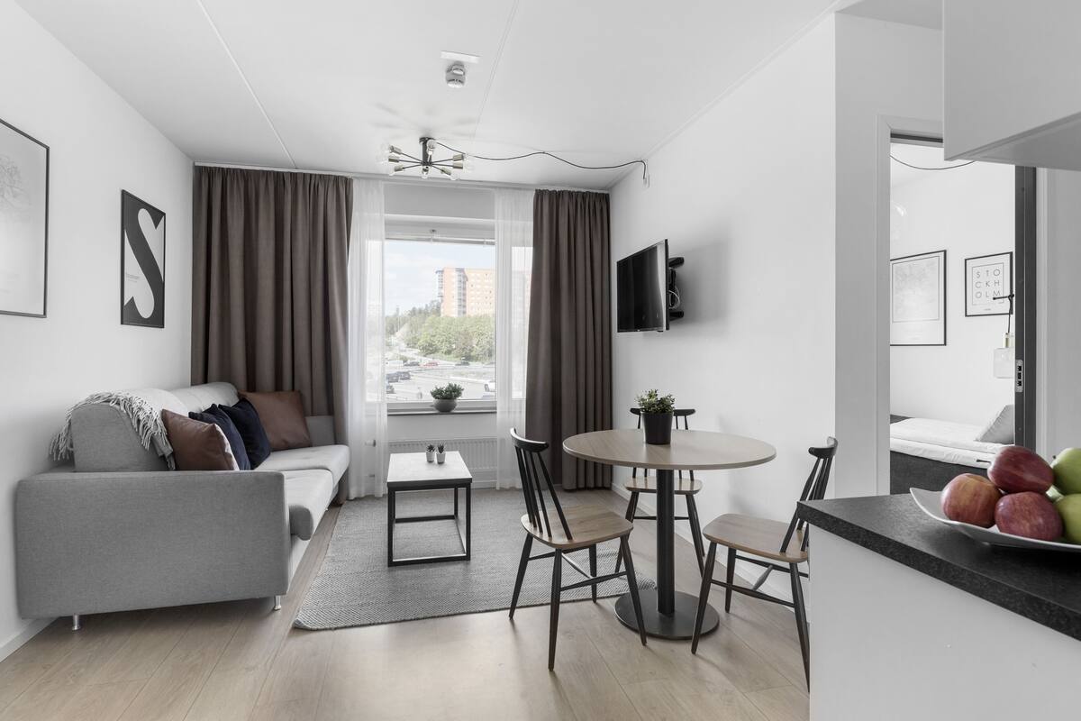 Un salon moderne avec un canapé, une table à manger et des chaises. Un téléviseur est fixé au mur et il y a une fenêtre avec des rideaux.