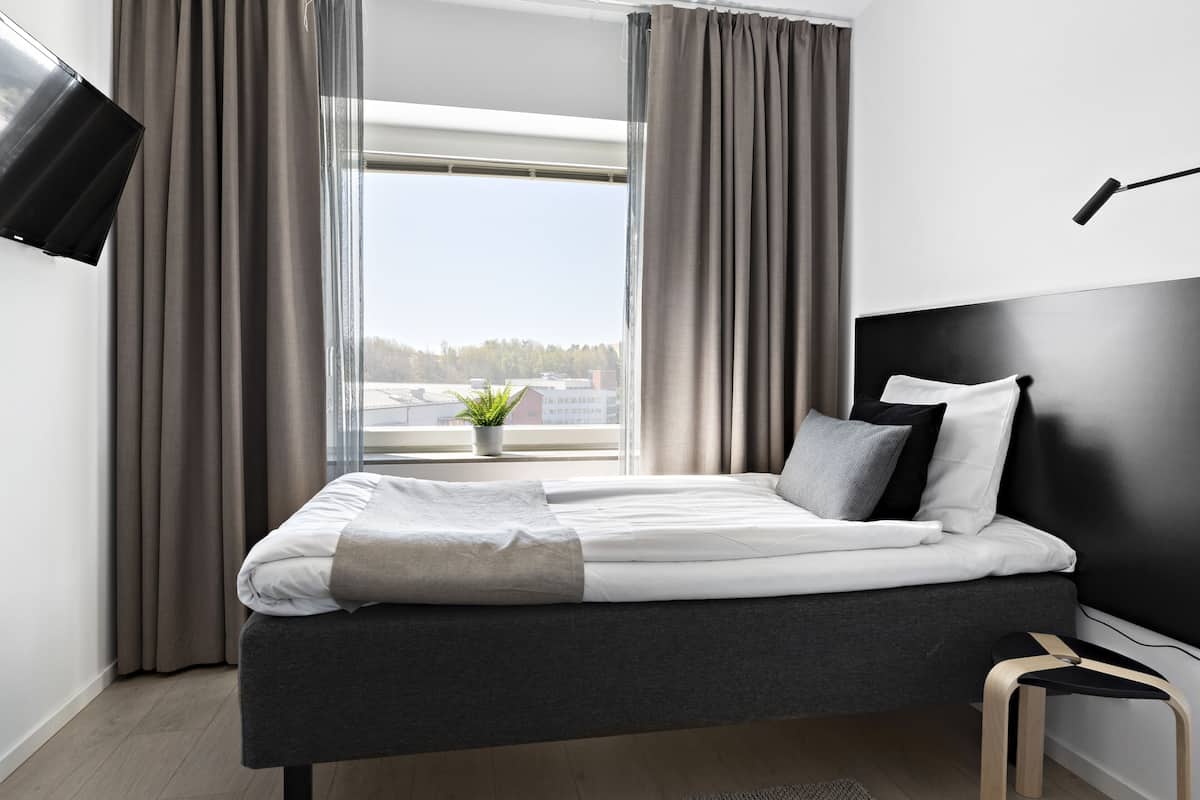 Une chambre moderne avec un lit, des rideaux, un téléviseur et une vue sur la ville.