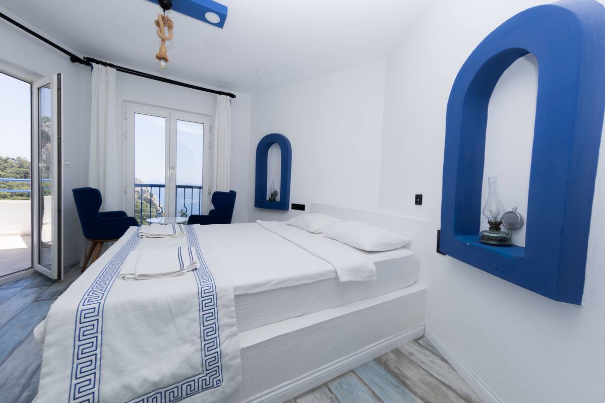 A bedroom with a bed, a blue arched window, and a balcony with a chair.