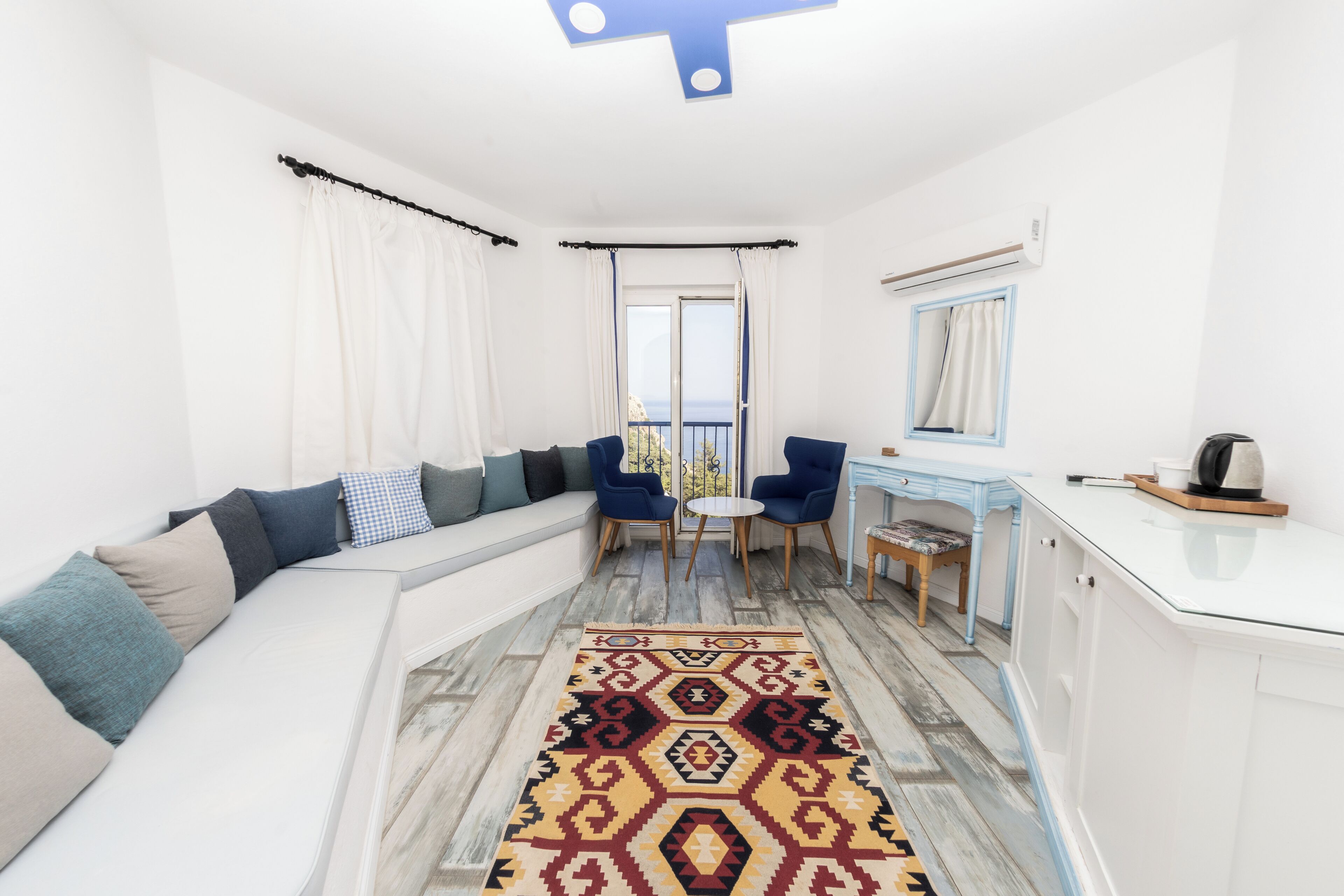 A modern living room with a white sofa, blue chairs, a patterned rug, and a view through a large window.