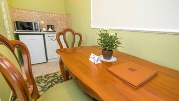 Un comedor con una mesa de madera, sillas, una planta en maceta, una pizarra y una kitchenette al fondo.