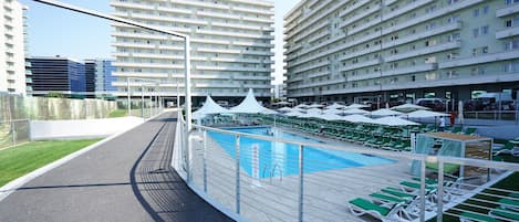 A rooftop pool area with a swimming pool, sun loungers, and a view of high-rise buildings.