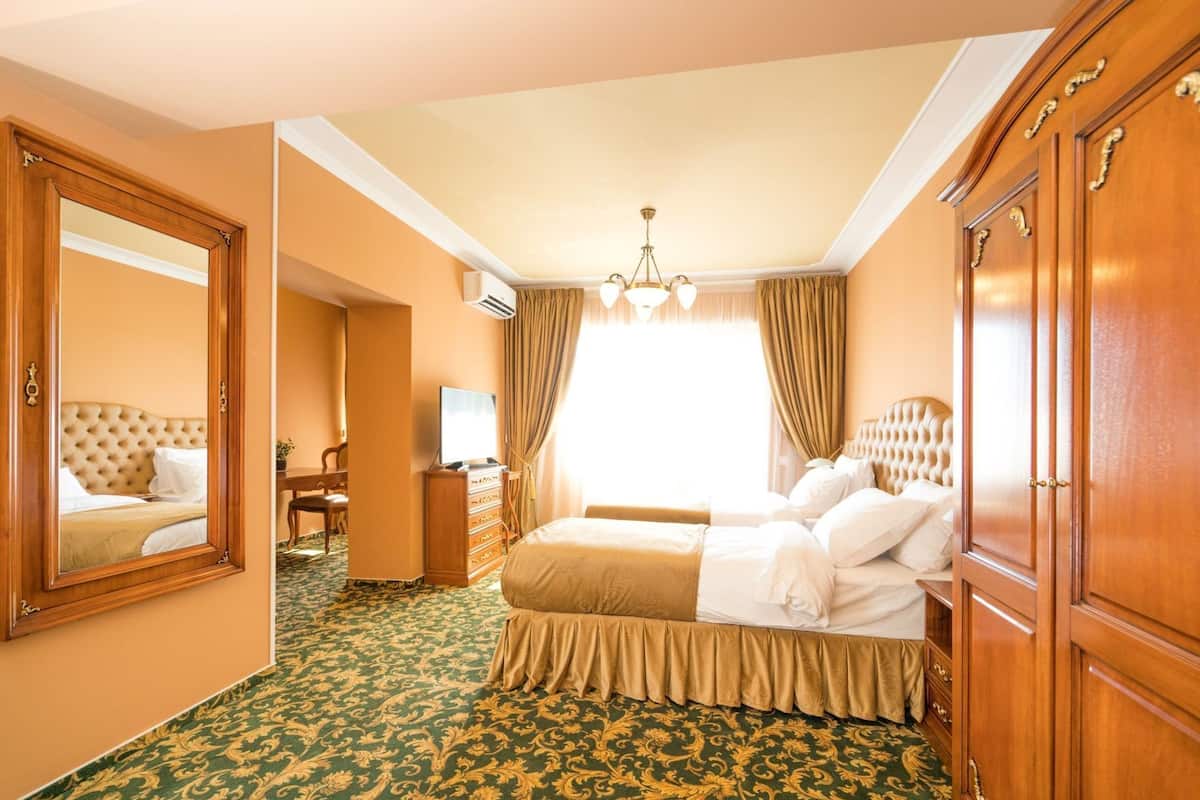 Une chambre d’hôtel avec un grand lit, une commode, un bureau avec une chaise, un miroir et un lustre.
