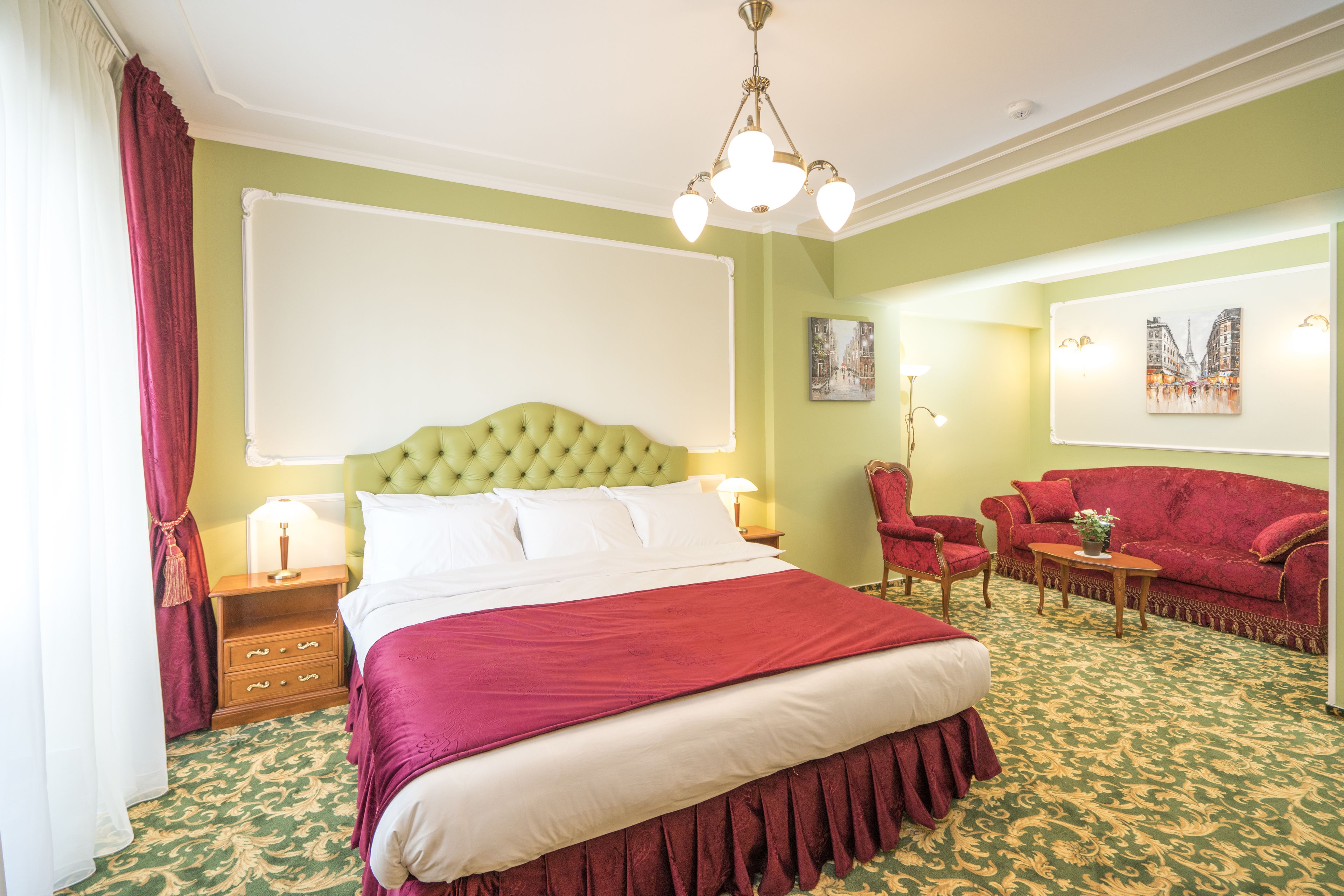 A hotel room with a large bed, a red sofa, a wooden nightstand, and a green patterned carpet.