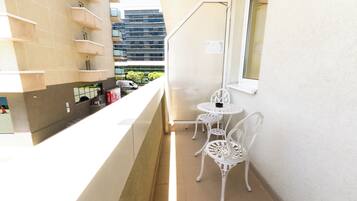 A narrow balcony with a kitchen area, two white metal chairs, and a window.