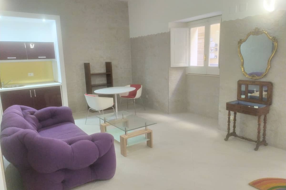 A room with a purple sofa, a small round table, and a mirror on the wall.