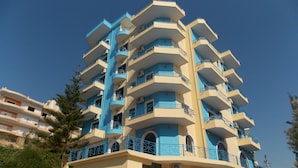 Um hotel com vários andares, varandas, uma escadaria que leva à entrada e um céu azul límpido.