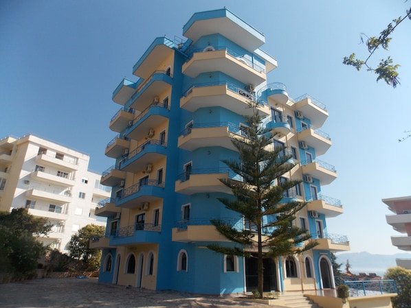 Un edificio de varios pisos con balcones, una escalera central y un árbol en la parte delantera.