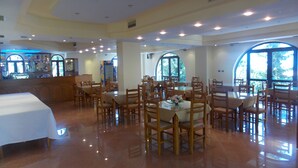 Uma sala de jantar espaçosa com várias mesas e cadeiras, grandes janelas e um bar.