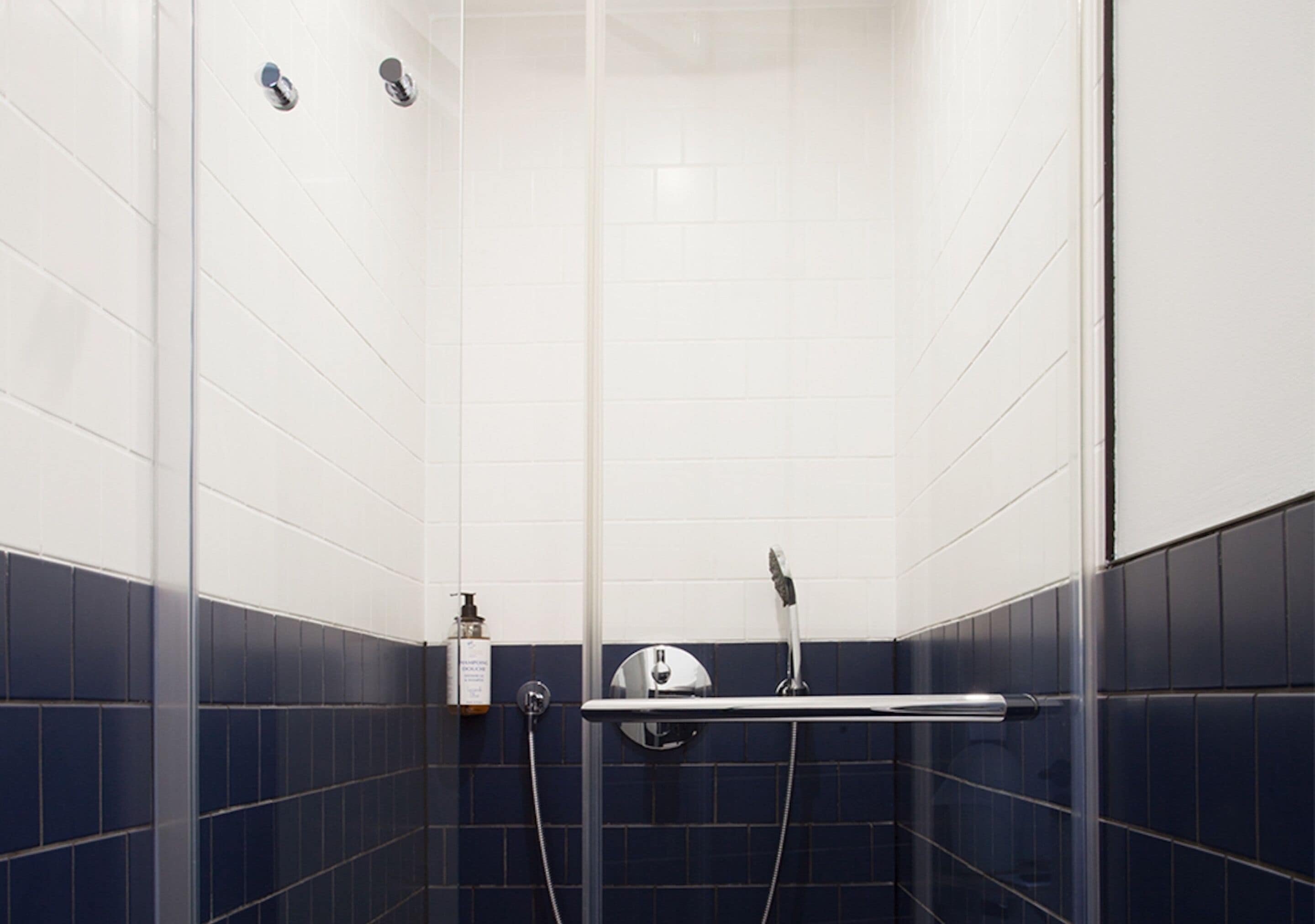 A shower with a glass door, a handheld showerhead, and a wall-mounted faucet.